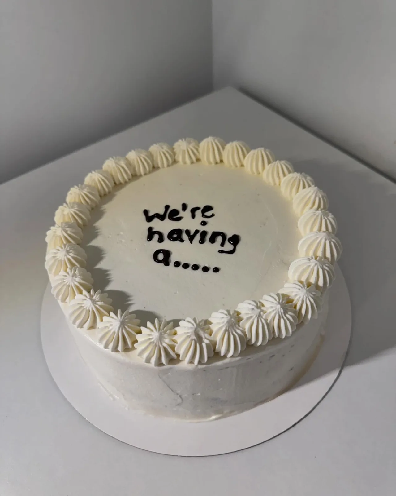 White piped celebration cake with a handwritten surprise announcement