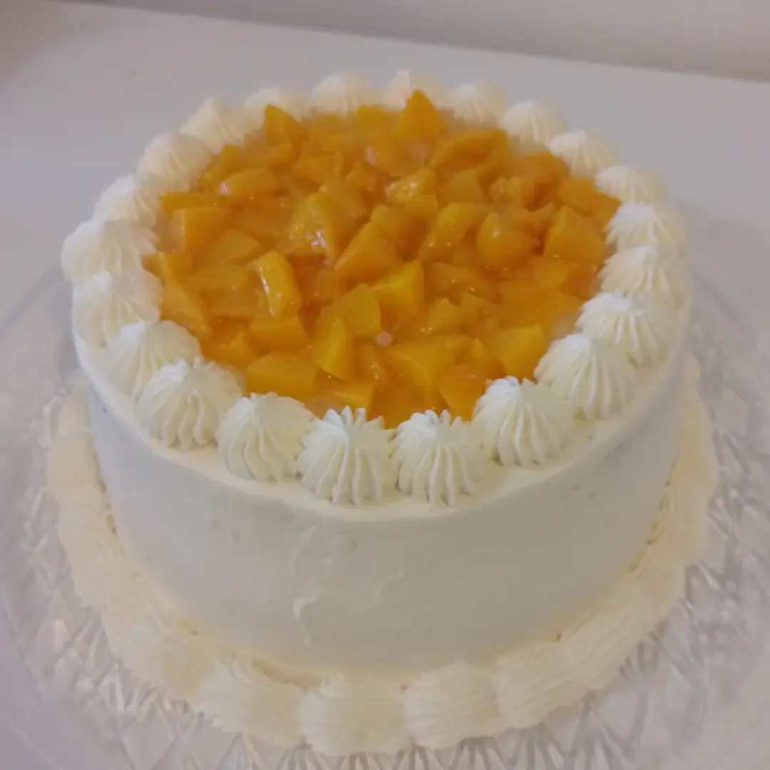 Round cream cake topped with fresh diced mango and a piped border