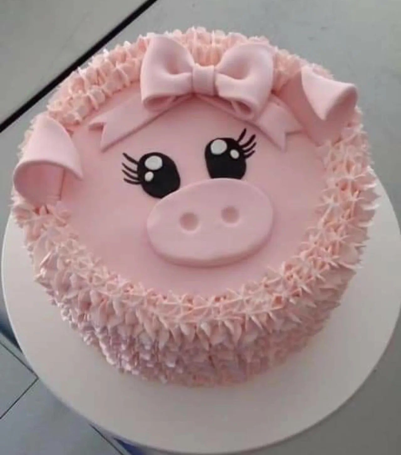 Pink buttercream cake decorated as a smiling pig with piped rosettes