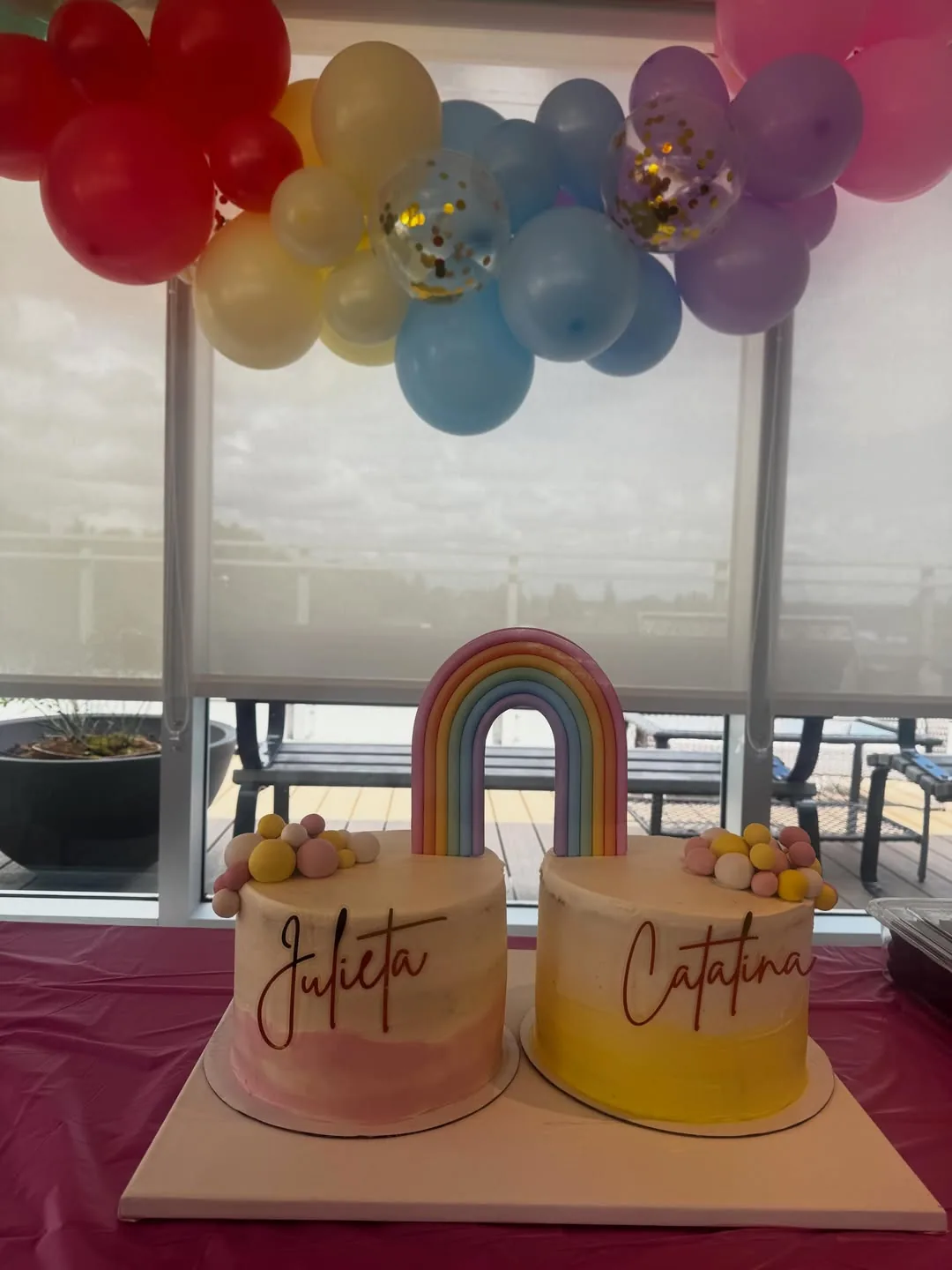 Two colourful custom cakes beneath a rainbow balloon display